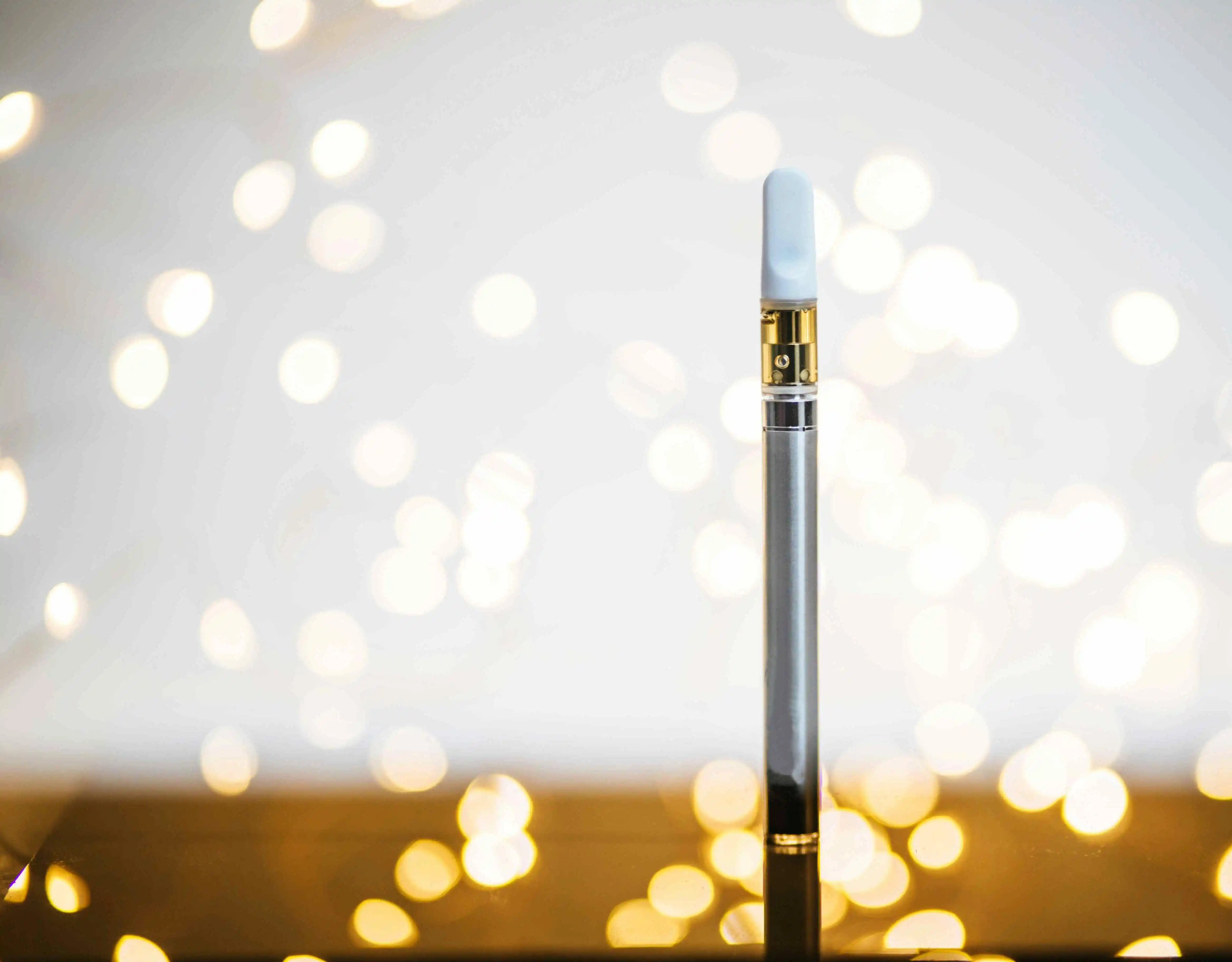 white thc dab pen standing upright against a background bright with lights