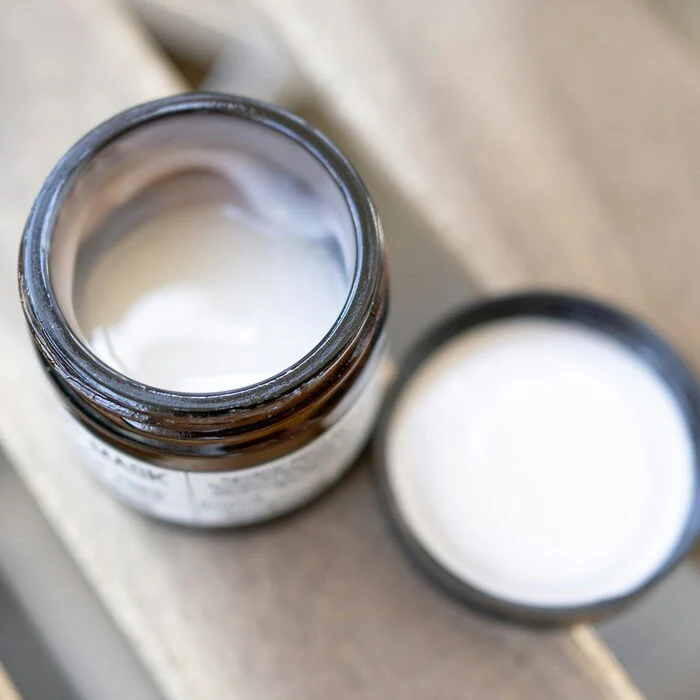 close up image of an open container of THC body cream by Proofly, sitting on a wooden bench